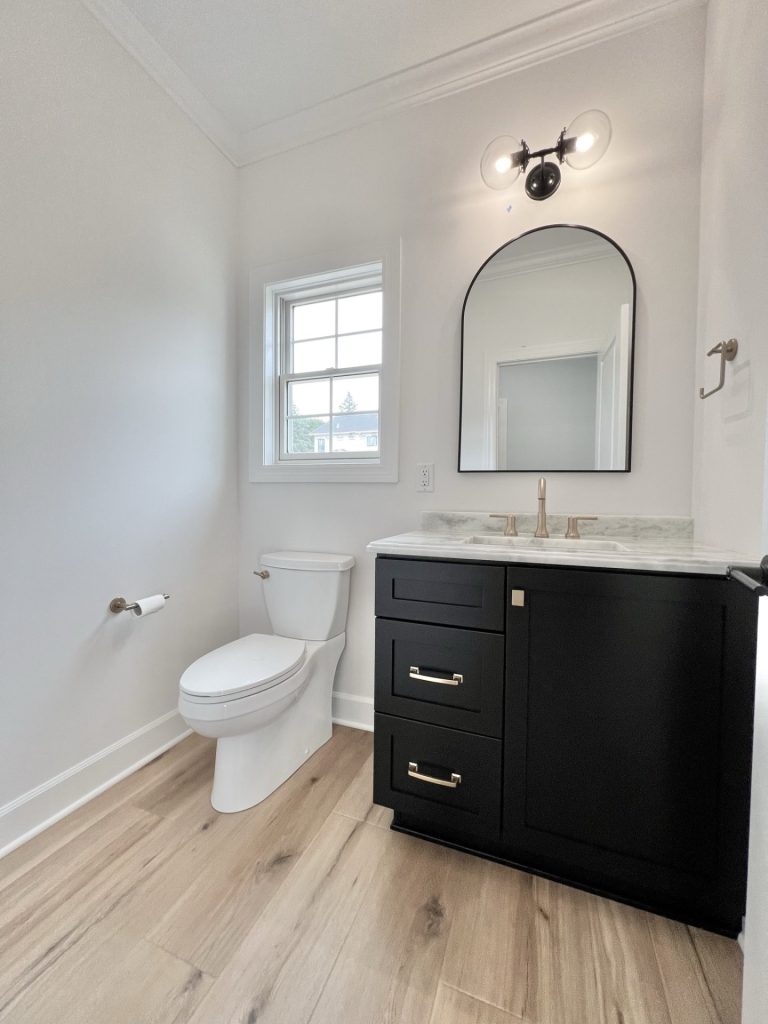 The Willow Downstairs Powder Room with Window, Mirror and Dark Cabinetry with White Walls and Wood Style Flooring
