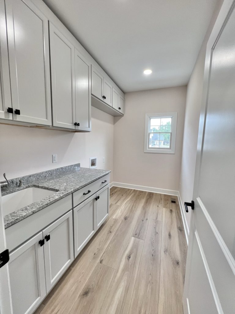 The Willow Laundry Room with White Cabinetry, Gray Granite Countertops, a Window, and Wood Style Flooring