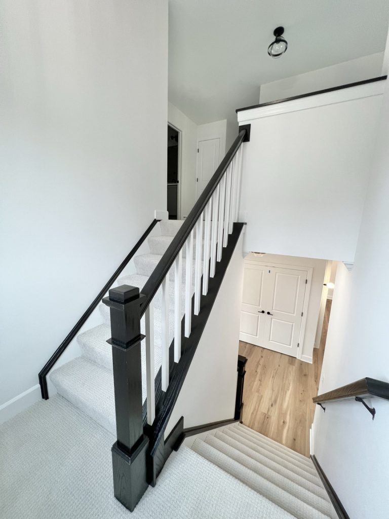 The Willow White Criss-Cross Stairway with White Carpet with Dark Railing to Downstairs with Wood Style Flooring
