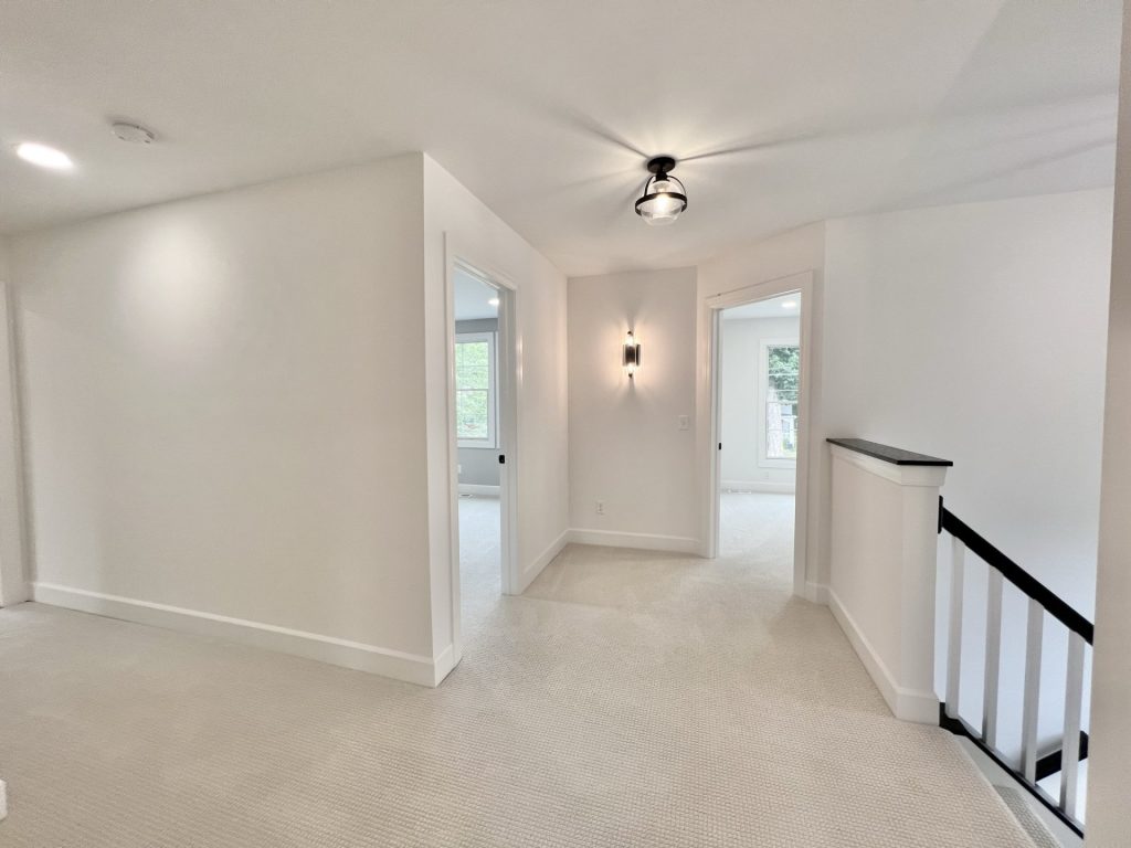 The Willow Upstairs Landing with Wall Sconce Looking into Two Bedrooms with Light Carpet