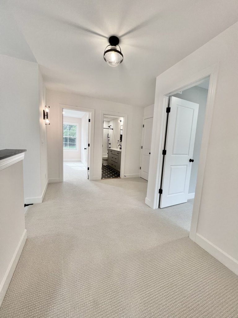 The Willow Upstairs Landing View of Master Bath and Bedroom with Overhead Lighting and Wall Sconce