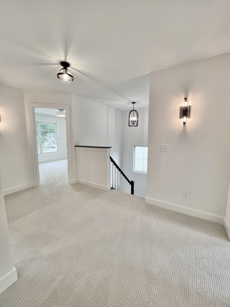 The Willow Upstairs Landing Looking Into Bedroom and Stairway with Wall Sconce and Overhead Lighting