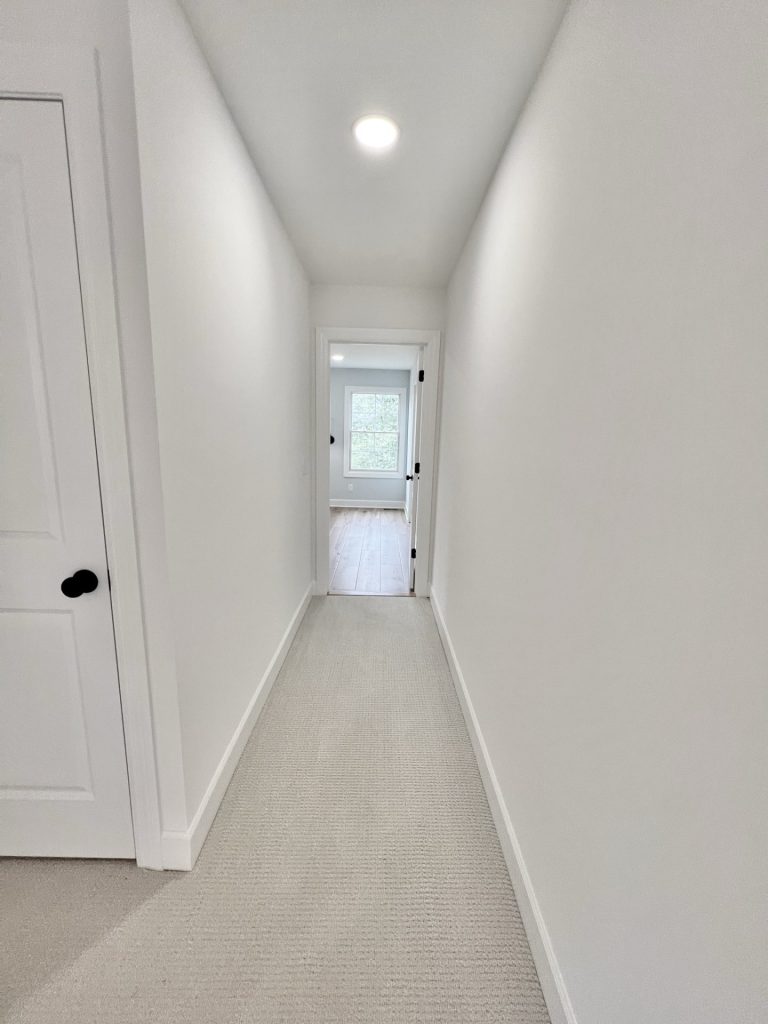 The Willow Upstairs Hallway with White Walls and Neutral Carpet Looking Into Bedroom with Window
