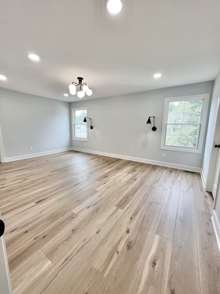 The Willow Master Bedroom in Pale Gray and White with Globe Chandelier, Wall Sconces, Two Windows and Wood Style Flooring