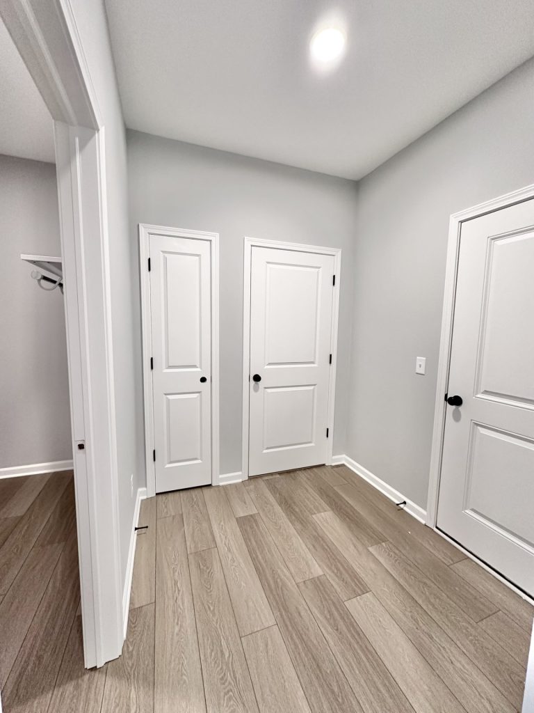 The Kendall Mudroom Hall with Wood-Look Flooring, White Doors, Gray Walls & Open Closet View