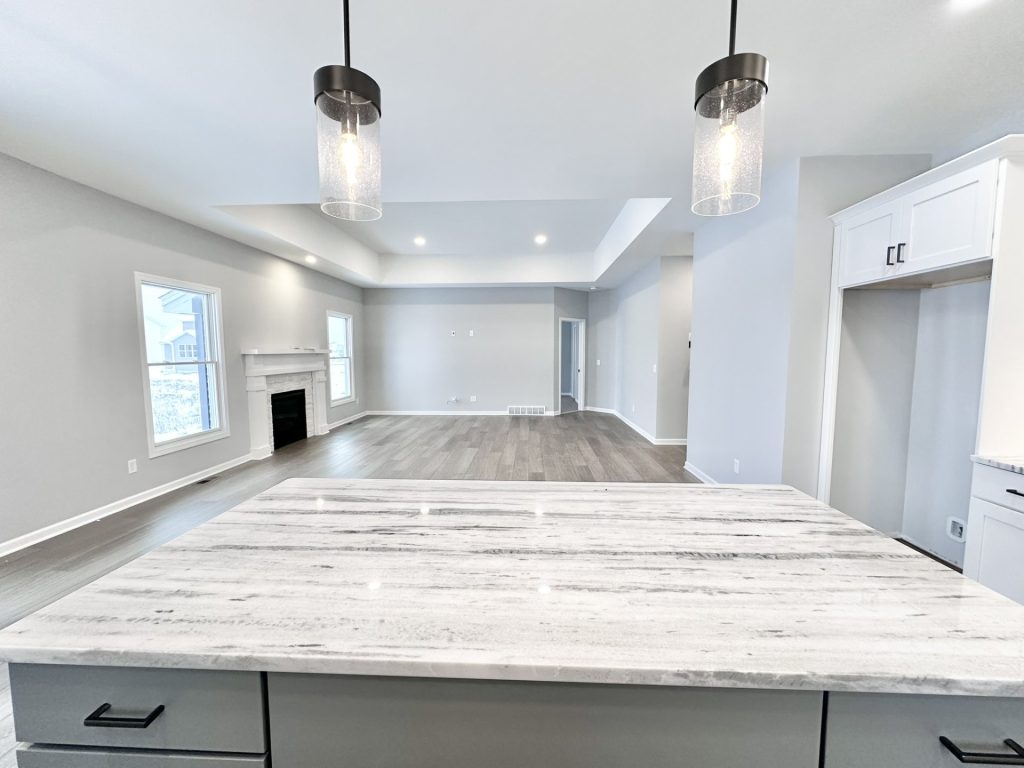 The Kendall Kitchen Island View to Great Room with Pendant Lights, Fireplace, Wood-Look Flooring & Open Layout