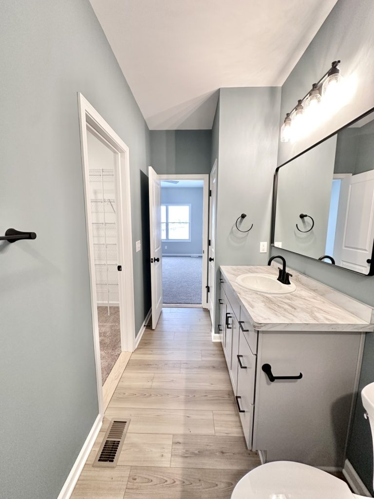 The Kendall Primary Bathroom with Gray Vanity, Walk-In Closet View, Tile Flooring & Black Fixtures