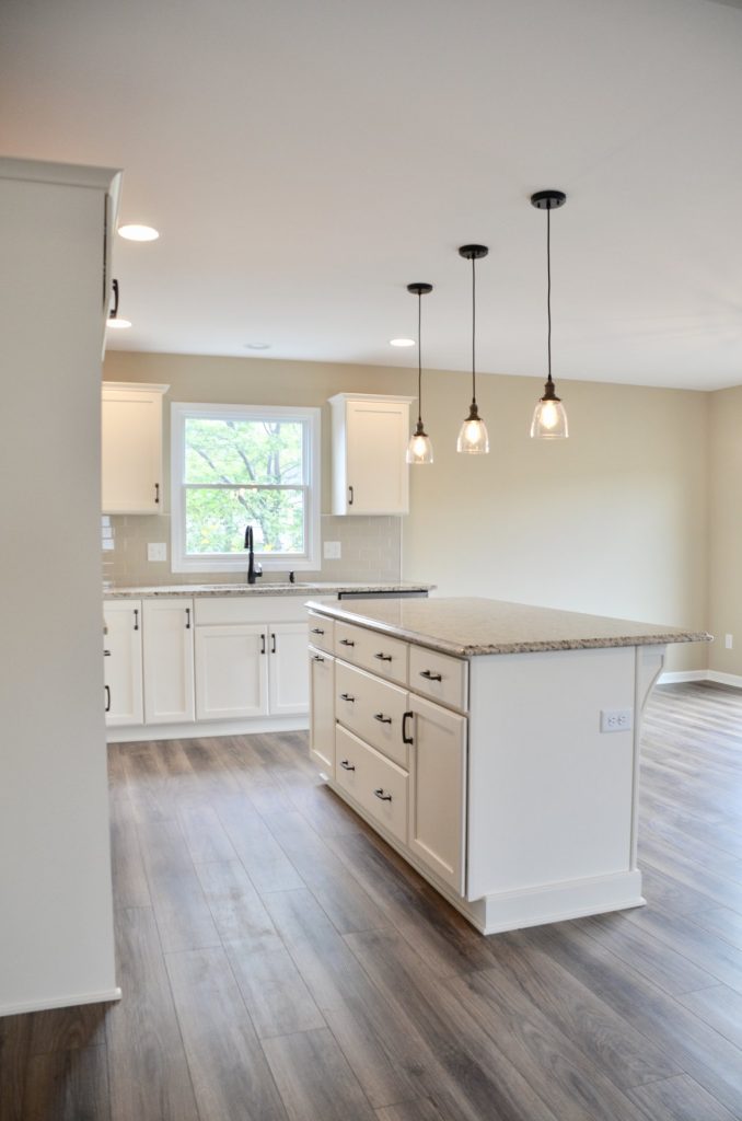 Baybrook-I-Kitchen-with-White-Cabinetry-Granite-Island-Pendant-Lighting-and-Wood-Look-Flooring