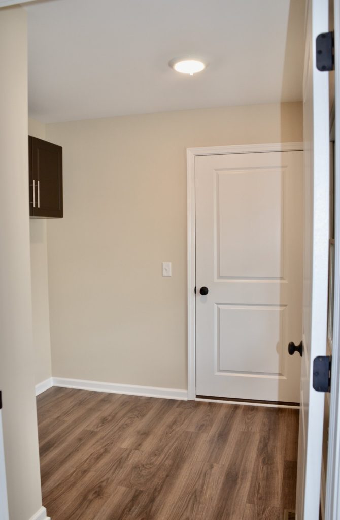 Baybrook-I-Mudroom-with-Wood-Look-Flooring-White-Door-and-Dark-Upper-Cabinet