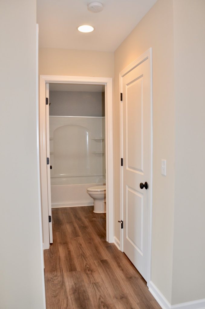 Baybrook-I-Hallway-with-Wood-Look-Flooring-White-Doors-and-Full-Bathroom-View