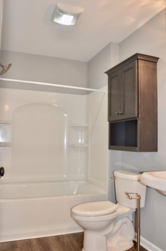 : Baybrook-I-Full-Bathroom-with-Tub-Shower-Combo-Dark-Wall-Cabinet-and-Wood-Look-Flooring