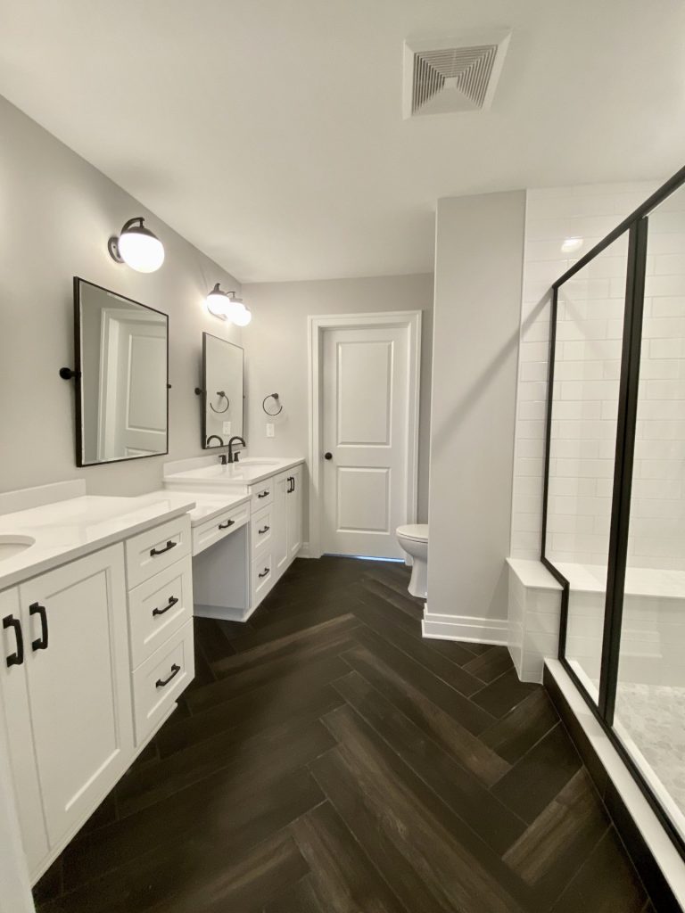 The Cooper II Primary Bathroom with Double Vanity, Glass Shower, Dark Herringbone Tile Floor & Black Fixtures