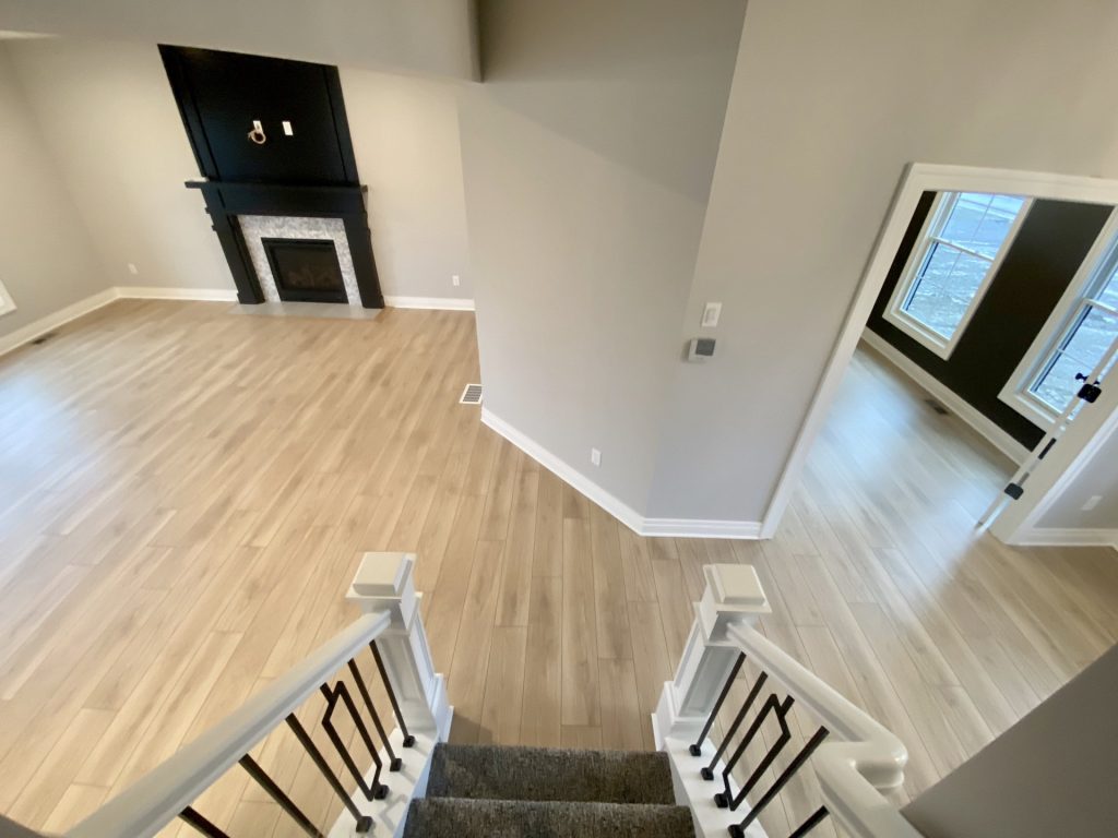 The Cooper II Staircase View to Great Room with Fireplace, Dark Accent Walls, Wood-Look Flooring & Den Entry