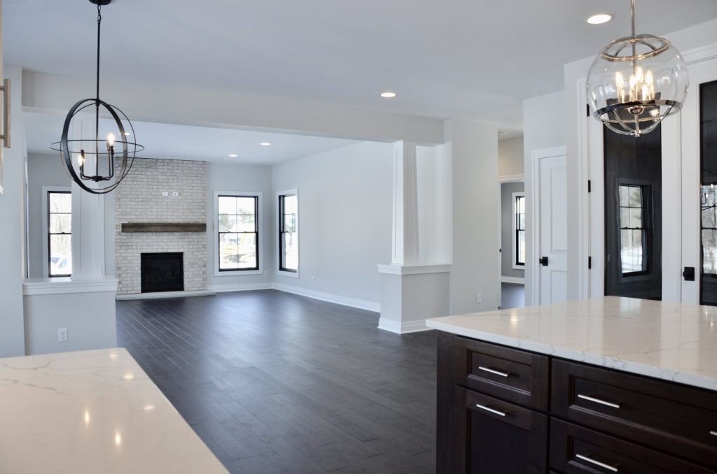 The Stratford II Great Room View From the Open Kitchen with Fireplace View, and Dark Wood Flooring