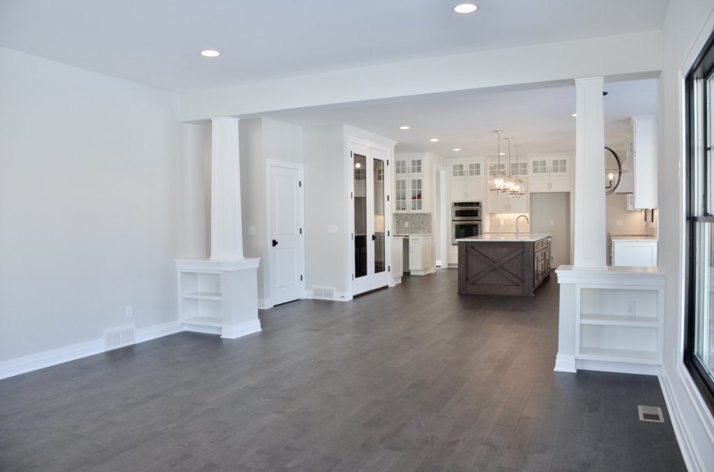 Great Room View to Kitchen with Columns, Island, Dark Wood Flooring & Open Layout