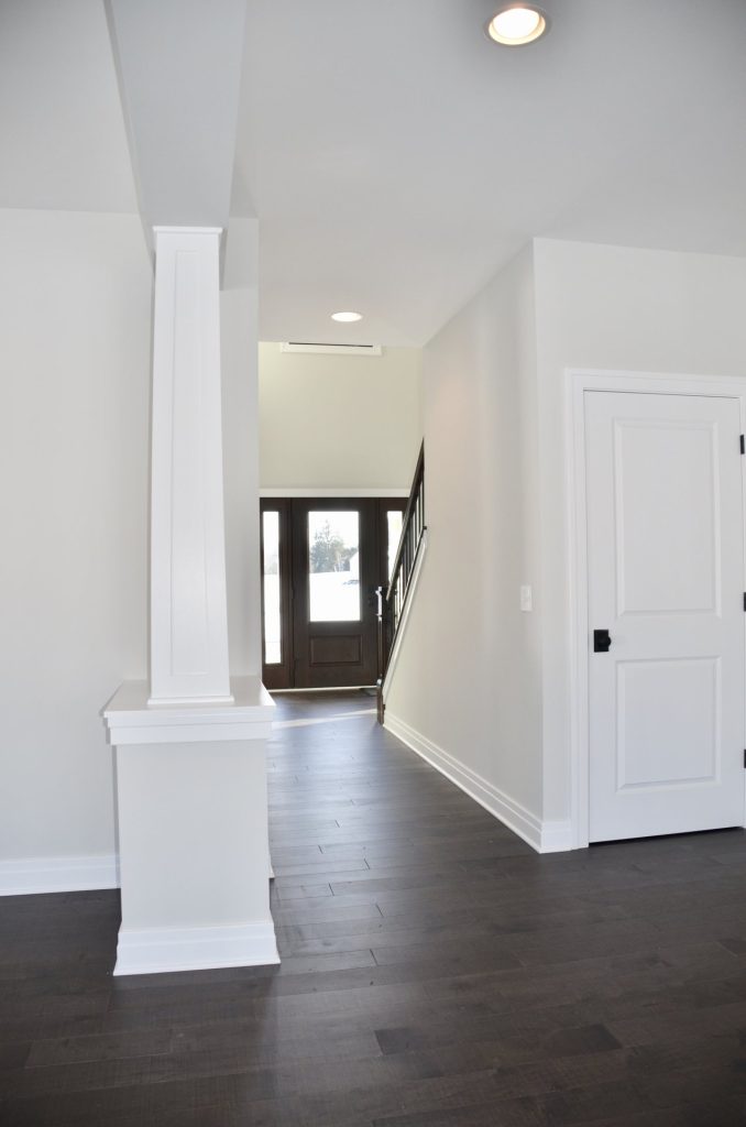 The Stratford II Hallway toward Front Entry with Columns, Dark Wood Flooring, Black Front Door & Staircase View