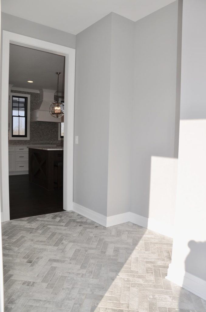 The Stratford II Front Hallway with Herringbone Tile Flooring, Gray Walls, White Trim & Kitchen Entry View