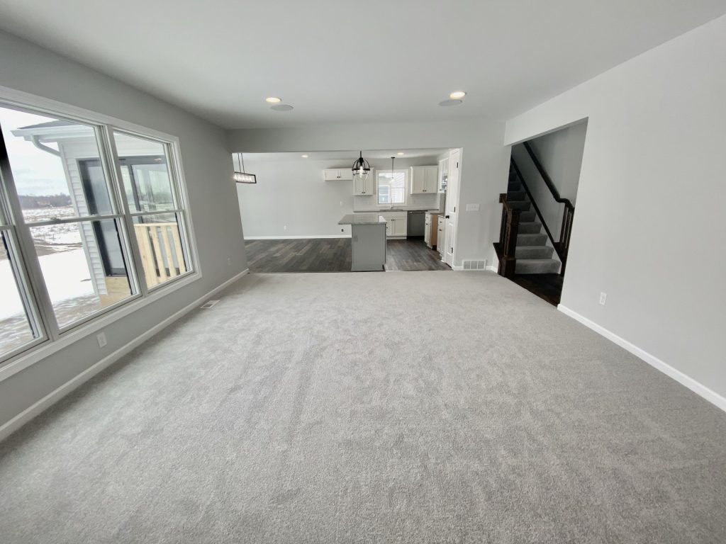 The Cooper I Great Room with Light Carpet, Staircase, Large Windows & Kitchen View