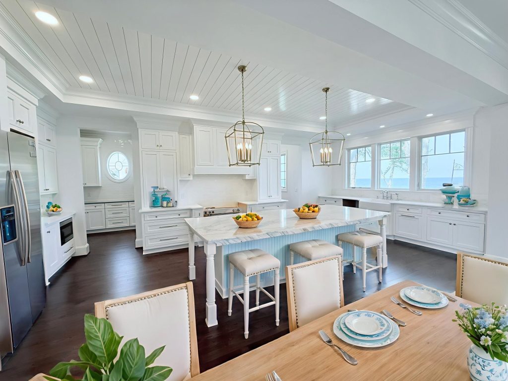 Coastal-style open kitchen with white cabinetry, a light blue island, brass lantern pendants, and a breakfast table set with blue-and-white dishware