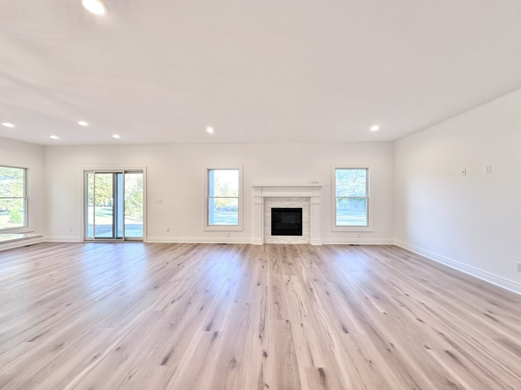 Open-concept living room with a stone-surround gas fireplace flanked by windows and a sliding glass door to the patio