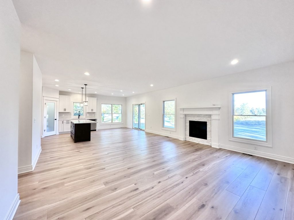 Open-concept living room with light wood flooring, stone fireplace, large windows, and a sliding glass patio door