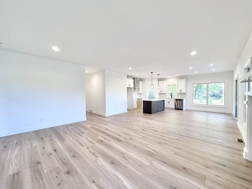 Open-concept great room and kitchen with light wood-look flooring, white cabinets, and a dark waterfall island