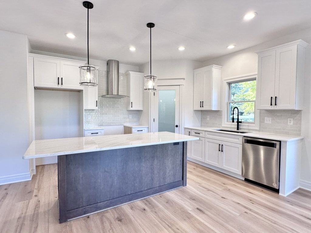Kitchen with white shaker cabinets, stainless range hood, dark waterfall island with white quartz top, and pendant lighting