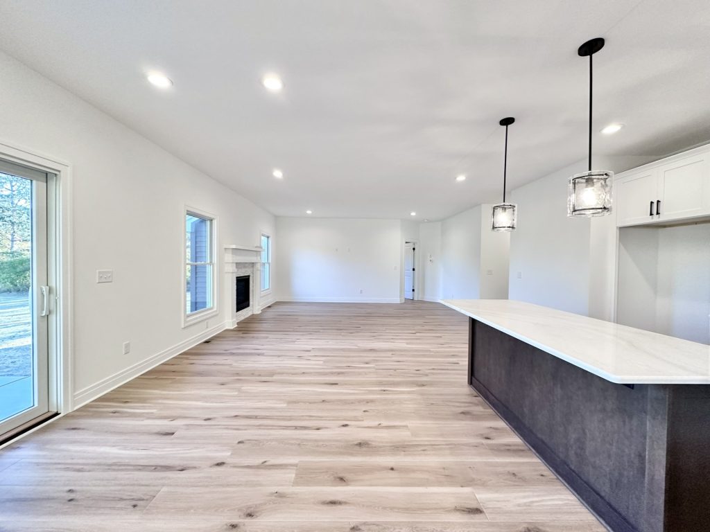 Open-concept great room with wood-look flooring, gas fireplace with stone surround, and sliding glass door to the patio