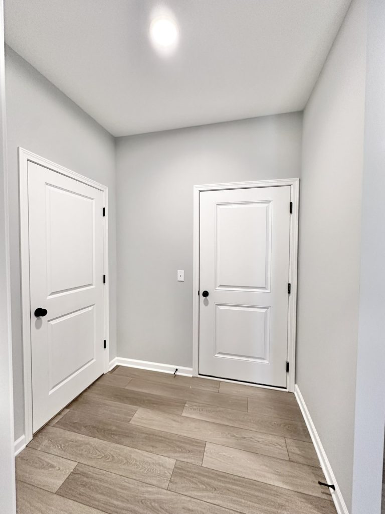 Empty mudroom hallway with wood-look flooring and white paneled doors leading to a closet and exterior entry