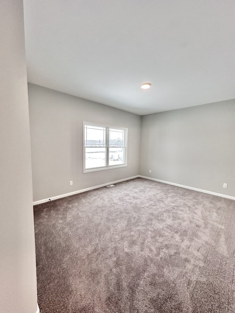 Empty bedroom with gray carpet, a window overlooking a snowy lot, and recessed ceiling light