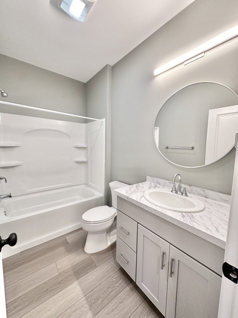 Bathroom with tub/shower combo, white oval sink vanity with marble-look countertop, and wood-look tile floor